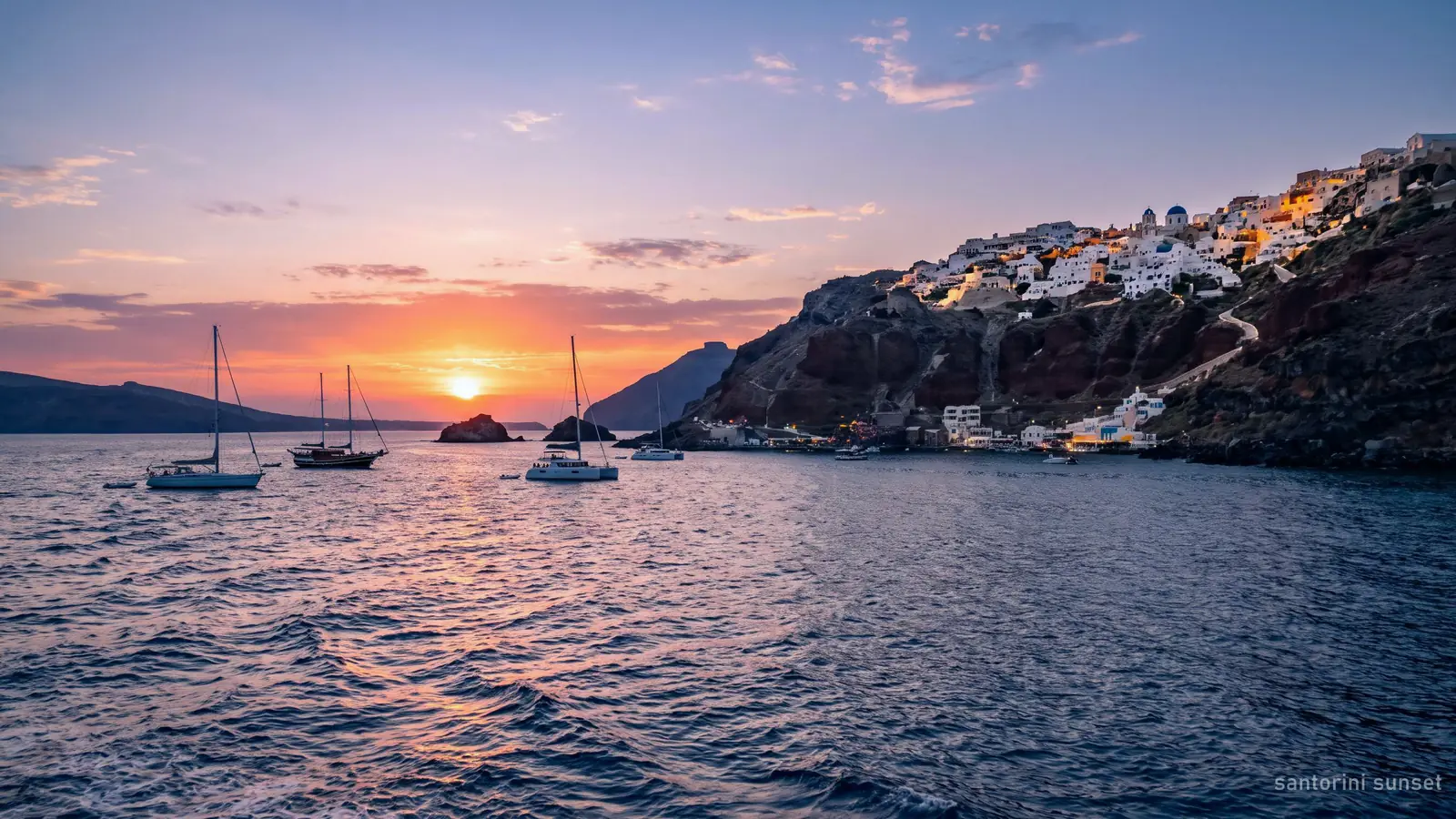 Sunset over the Aegean from the water below Oia, the white village on the cliff above